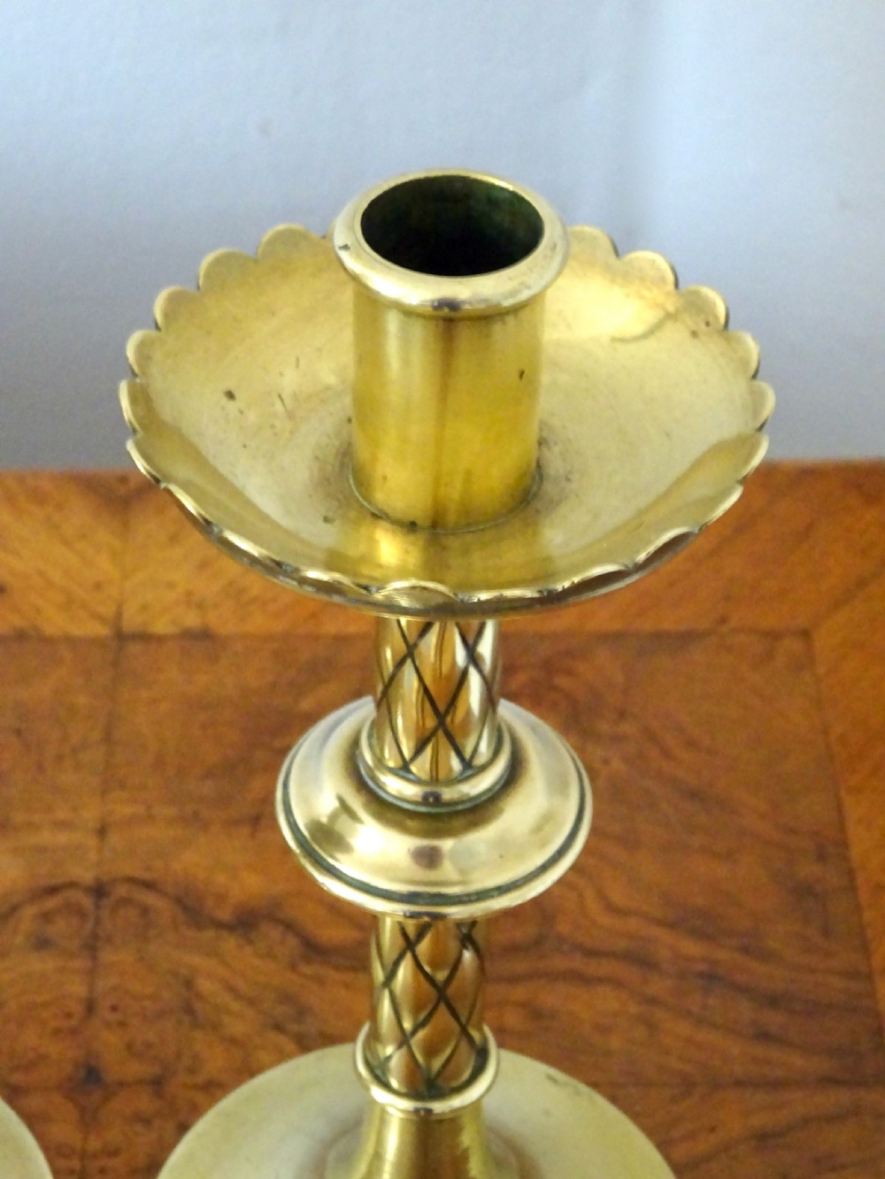 A pair of turned Victorian brass candlesticks featuring diamond-engraved stems, scalloped drip pans, and circular bases. View V