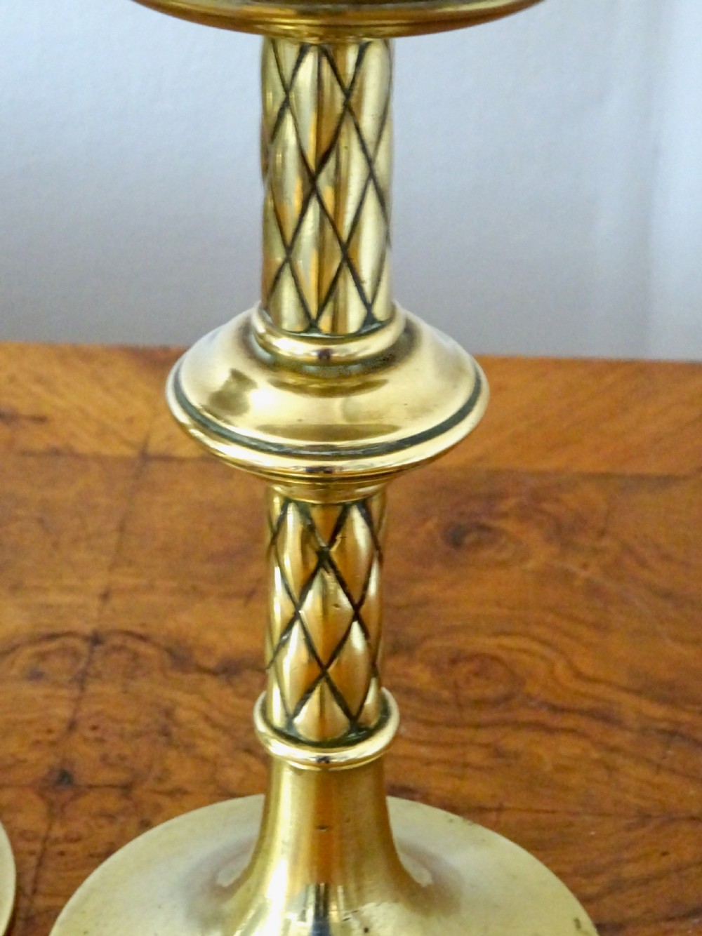 A pair of turned Victorian brass candlesticks featuring diamond-engraved stems, scalloped drip pans, and circular bases. View VII
