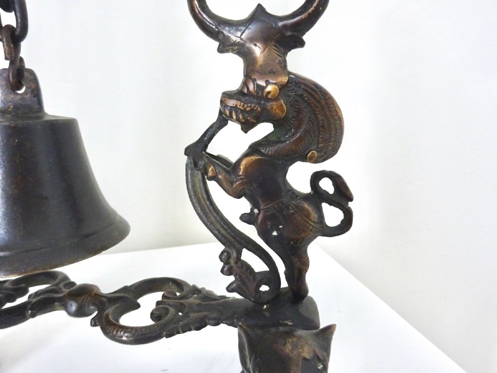 An ornate dark bronze table bell suspended by a chain from a cast arch frame with elephant bases and mythical figure uprights. View VII