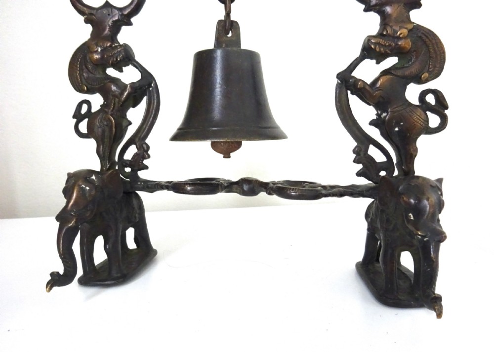 An ornate dark bronze table bell suspended by a chain from a cast arch frame with elephant bases and mythical figure uprights. View VIII