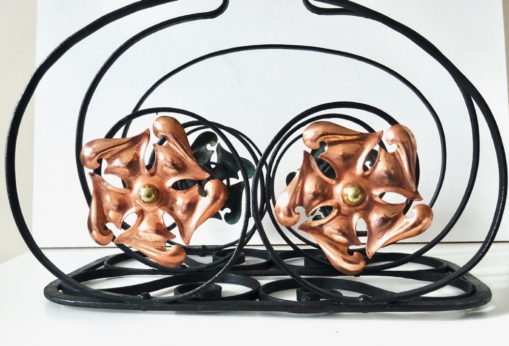 An Arts and Crafts wrought iron music rack featuring curved wire dividers, a twisted handle, and stamped copper flower motifs on the front. View VI