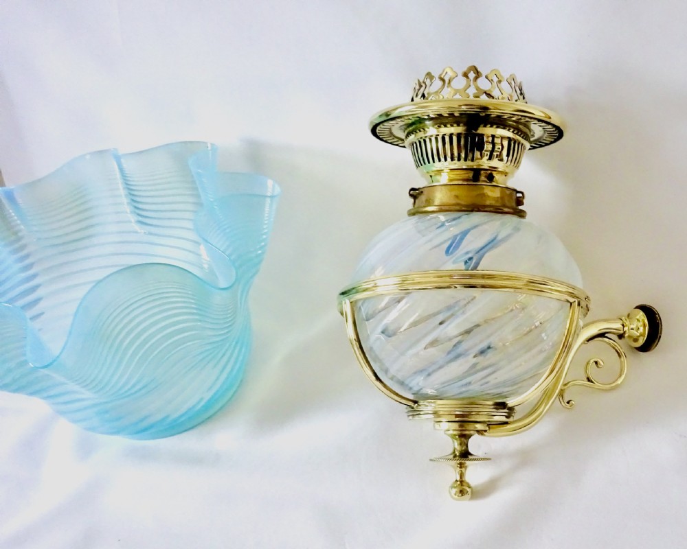 A Victorian brass wall-mounted oil lamp with a swirling blue glass reservoir held in a metal frame alongside a crimped blue glass shade.