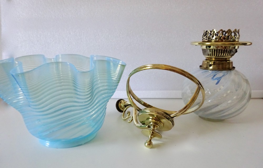 A Victorian brass wall-mounted oil lamp with a swirling blue glass reservoir held in a metal frame alongside a crimped blue glass shade. View VIII