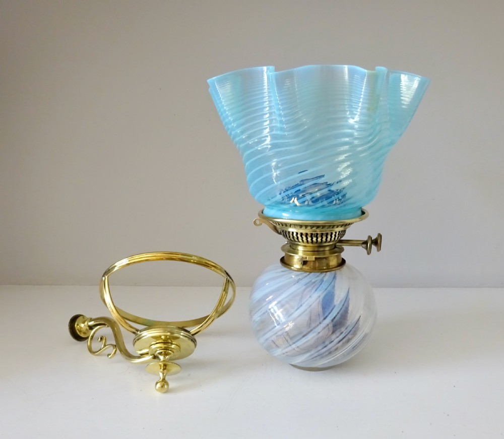 A Victorian brass wall-mounted oil lamp with a swirling blue glass reservoir held in a metal frame alongside a crimped blue glass shade. View XIII