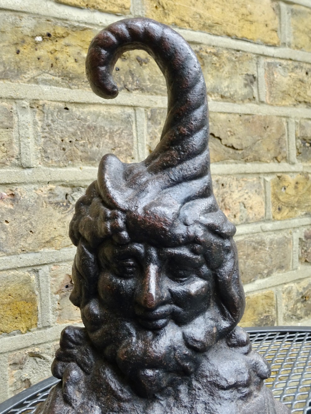 A Victorian cast iron doorstop featuring a molded figure of Punch with a tall curved cap forming a handle set on a stepped base. View II