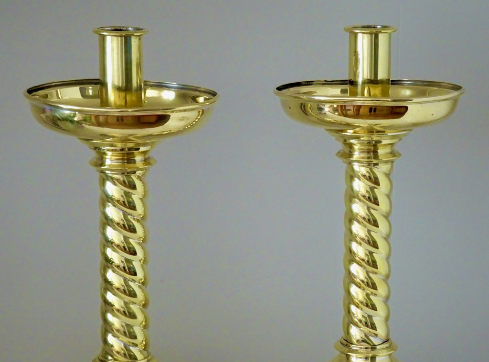 A pair of polished brass candlesticks with barley twist stems, broad drip pans, and domed bases set on small ball feet. View VI
