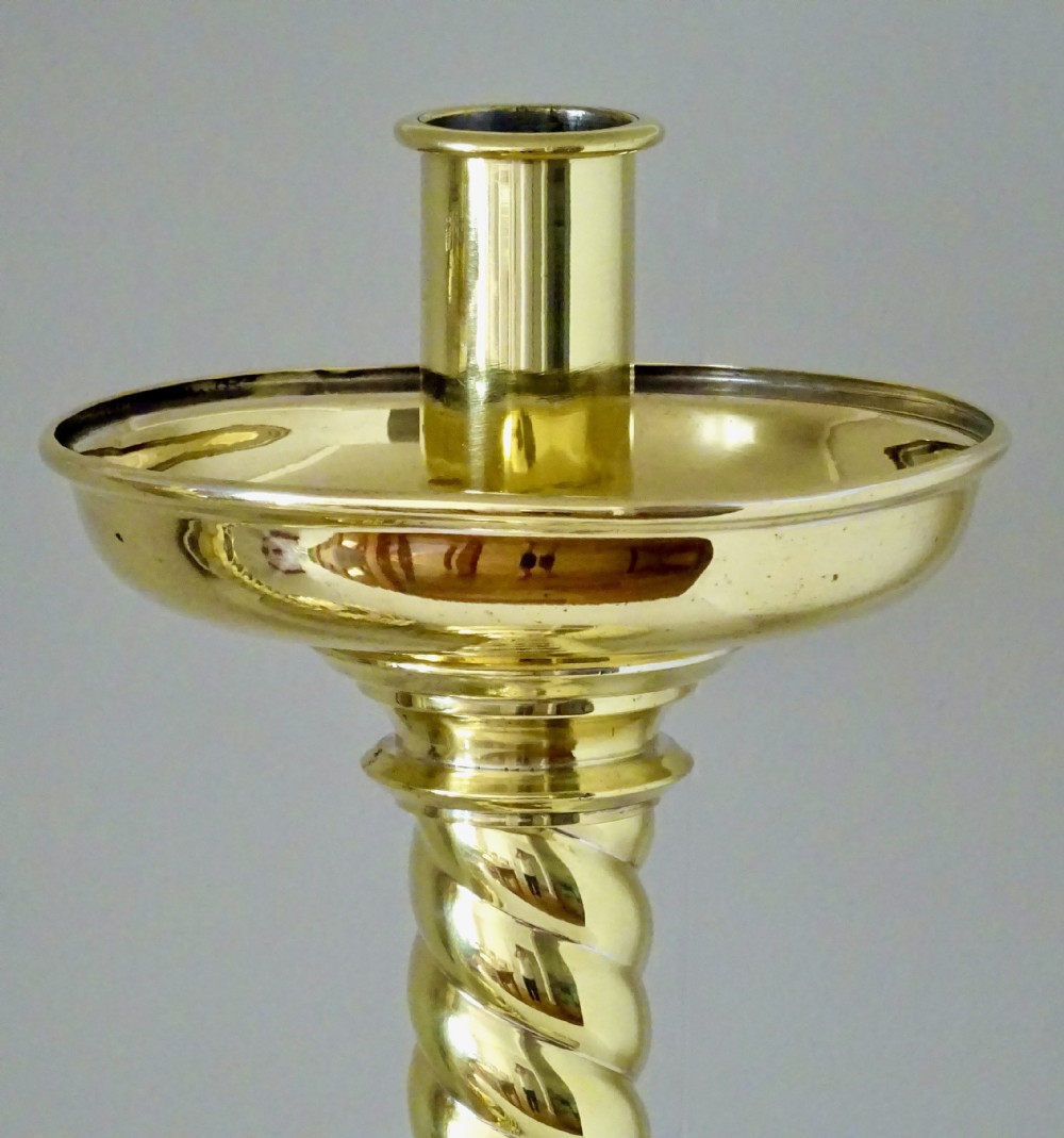 A pair of polished brass candlesticks with barley twist stems, broad drip pans, and domed bases set on small ball feet. View XII