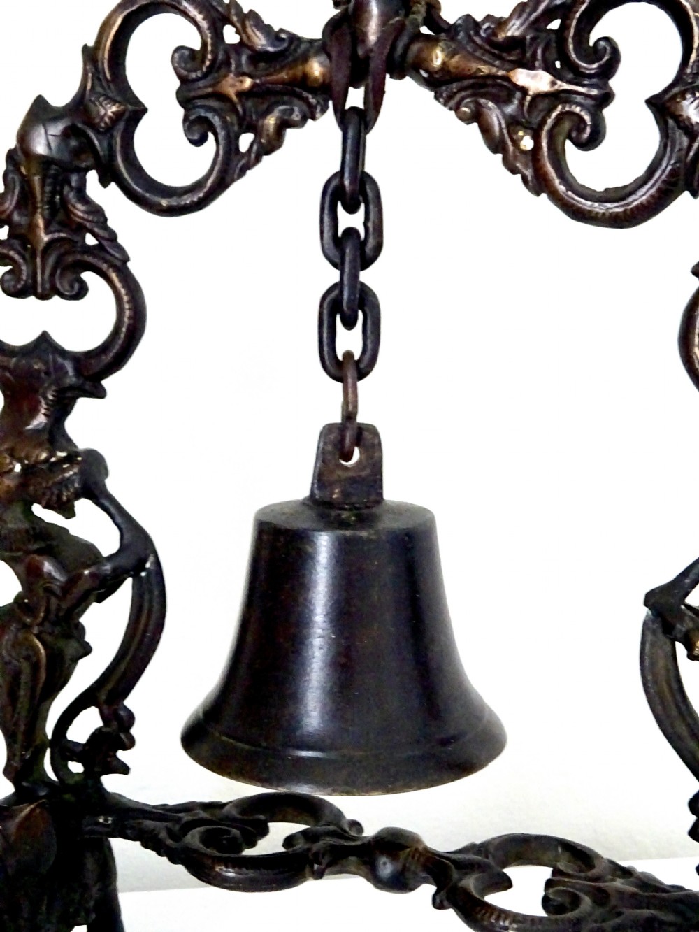 An ornate dark bronze table bell suspended by a chain from a cast arch frame with elephant bases and mythical figure uprights. View II
