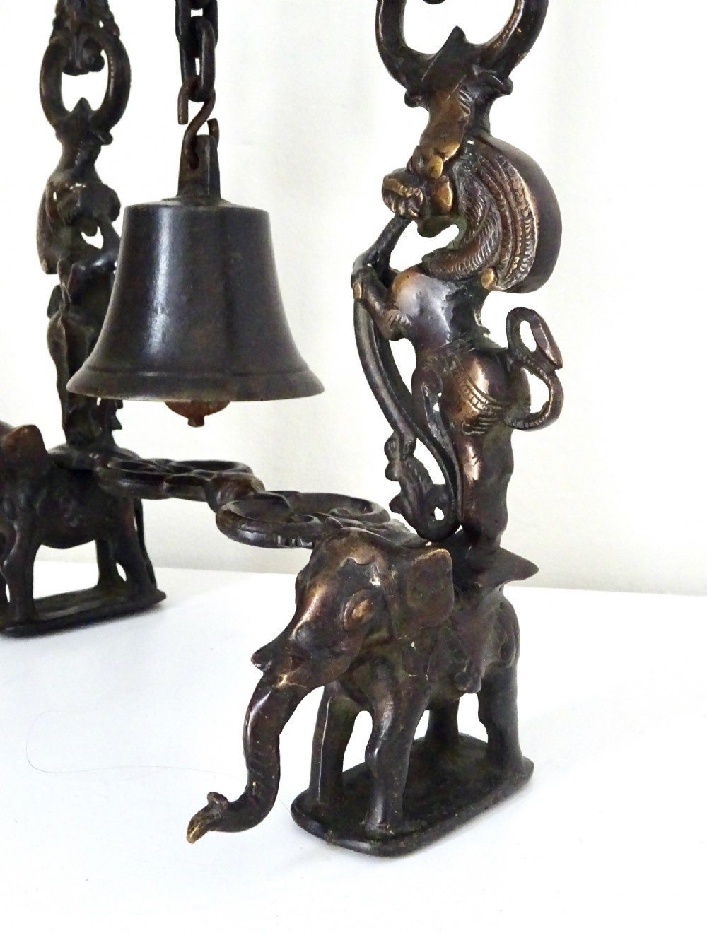 An ornate dark bronze table bell suspended by a chain from a cast arch frame with elephant bases and mythical figure uprights. View III