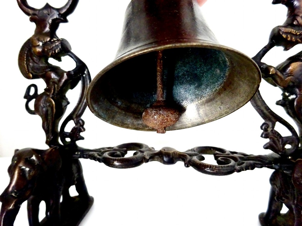 An ornate dark bronze table bell suspended by a chain from a cast arch frame with elephant bases and mythical figure uprights. View V