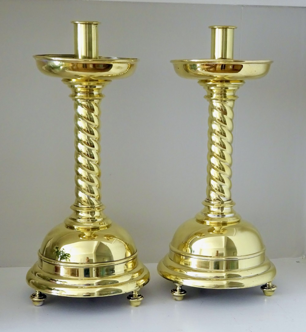 A pair of polished brass candlesticks with barley twist stems, broad drip pans, and domed bases set on small ball feet.