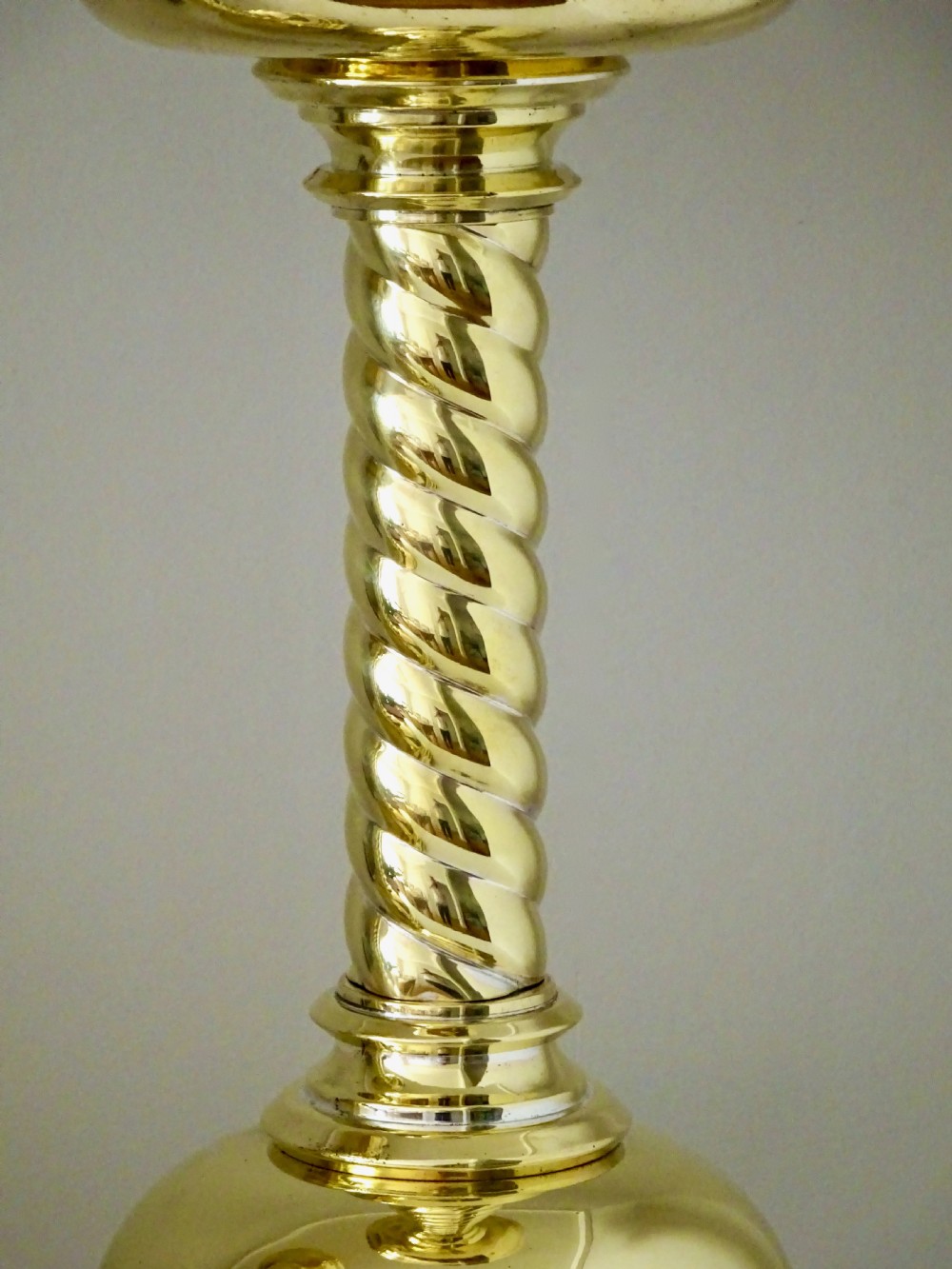 A pair of polished brass candlesticks with barley twist stems, broad drip pans, and domed bases set on small ball feet. View X