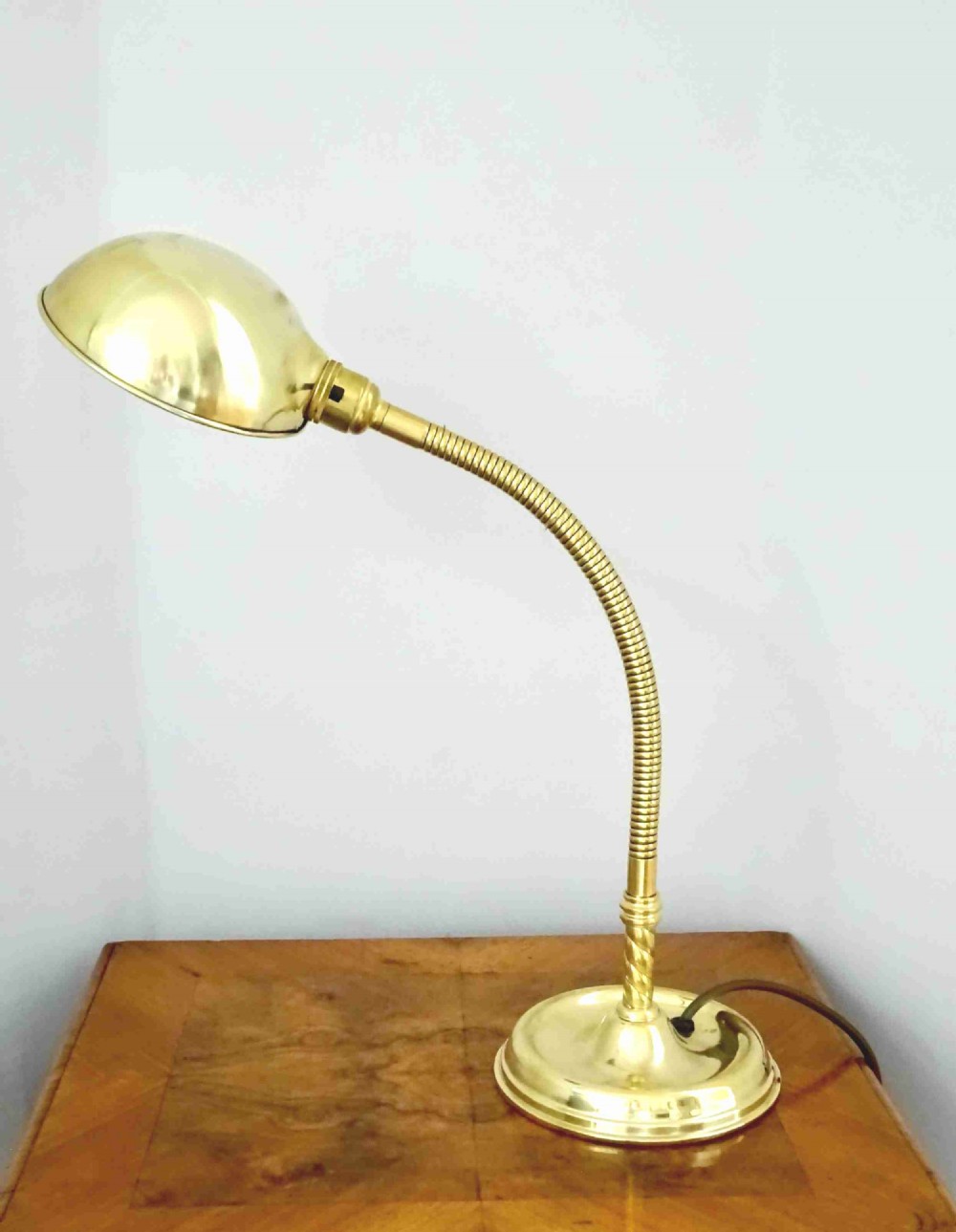 An Art Deco polished brass gooseneck desk lamp featuring an adjustable flexible arm, domed shade, and round stepped base.