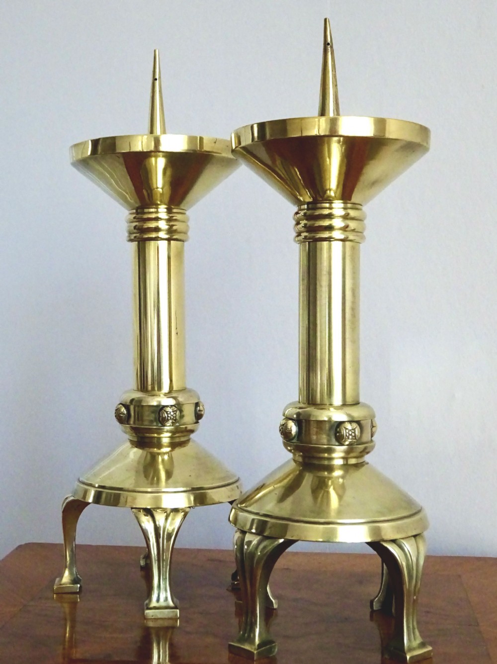 A pair of polished late Victorian brass pricket candlesticks featuring vertical spikes, flared drip pans, embossed stem knops, and tripod feet.