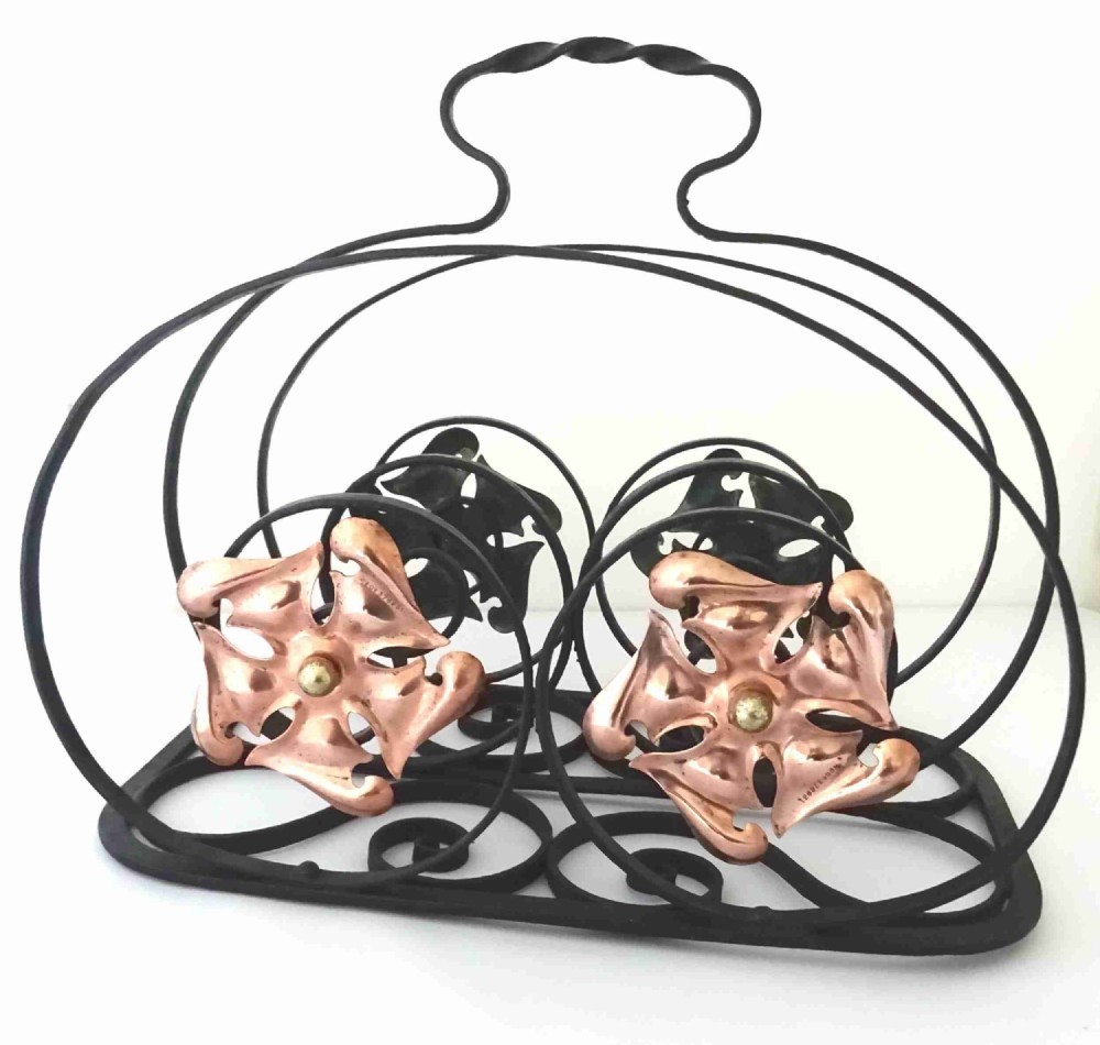 An Arts and Crafts wrought iron music rack featuring curved wire dividers, a twisted handle, and stamped copper flower motifs on the front.