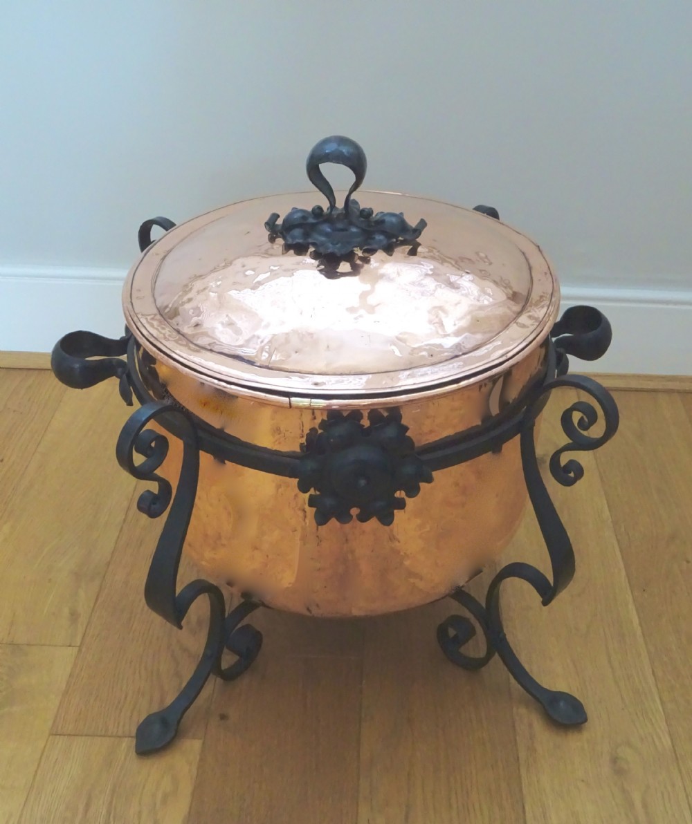 A large hammered copper bin with a domed lid fitted inside a black wrought iron stand with scrolled legs. View VII