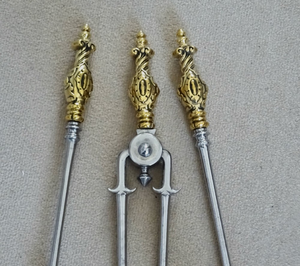 A set of three late nineteenth-century polished steel fire tools featuring ornate cast brass finial handles. View II