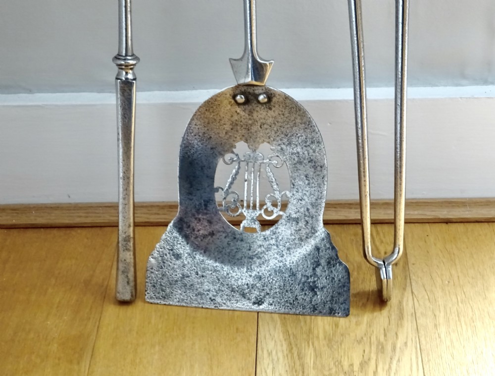 A set of three late nineteenth-century polished steel fire tools featuring ornate cast brass finial handles. View VI