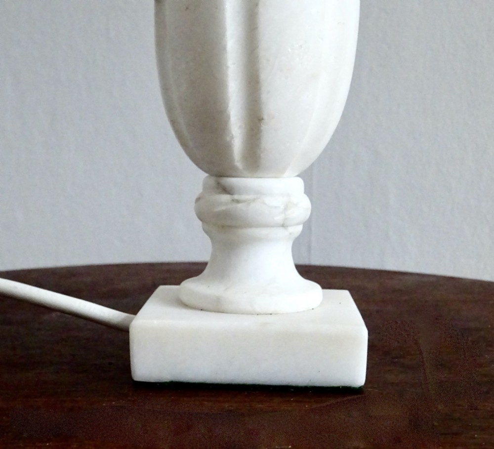 A small carved white marble table lamp base shaped like a classical urn resting on a square plinth. View II