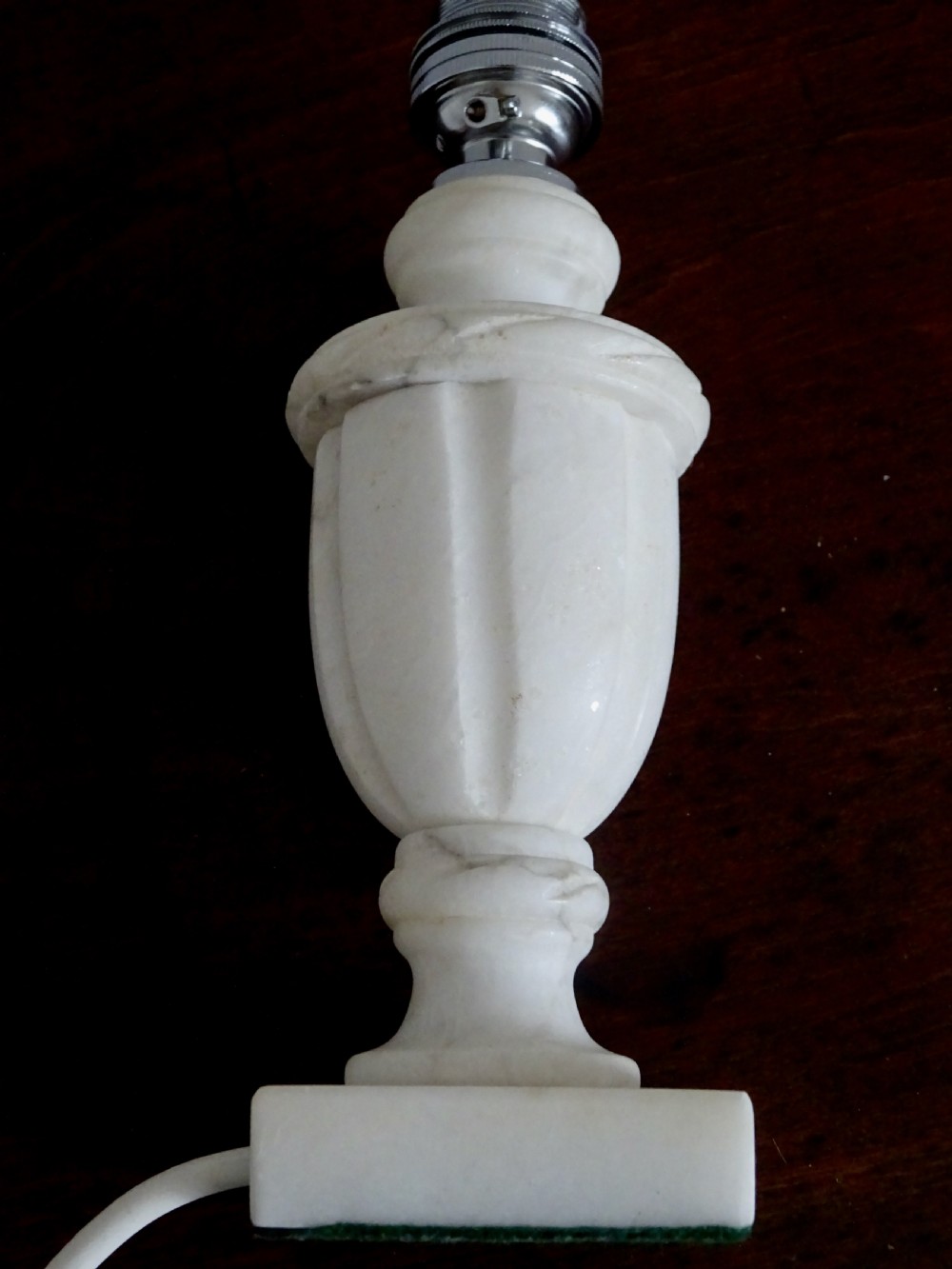 A small carved white marble table lamp base shaped like a classical urn resting on a square plinth. View V