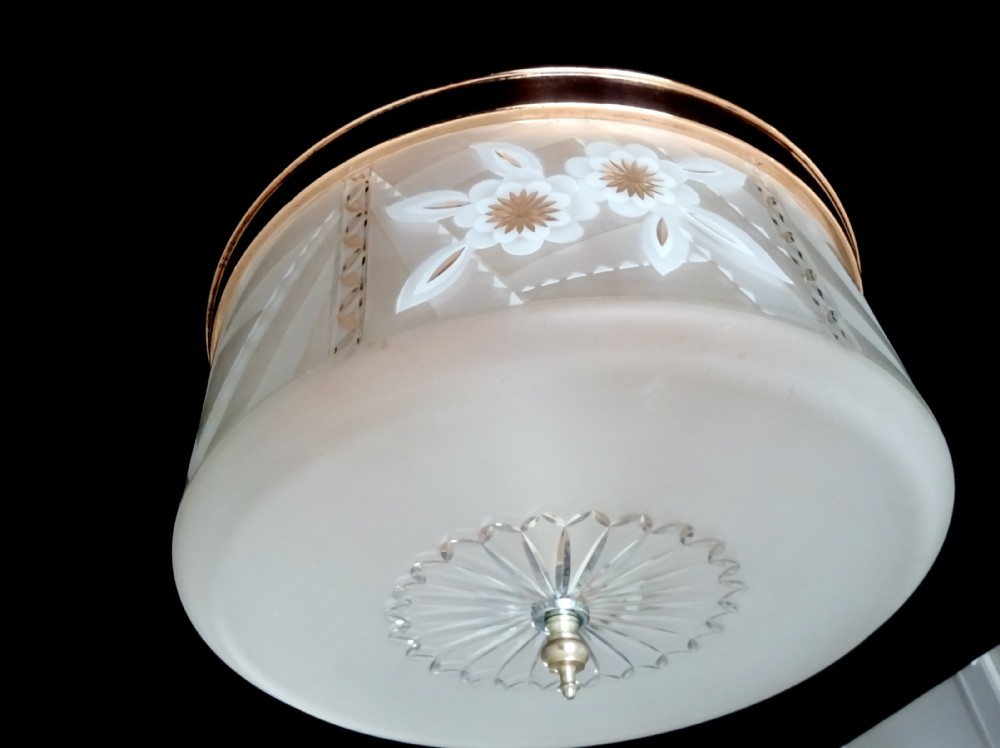 A circular 1930s flush mount ceiling light made of frosted glass featuring etched floral details and a polished copper gallery rim.