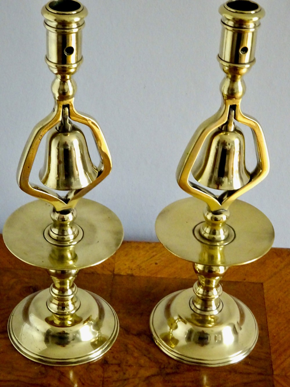 A pair of Victorian polished brass tavern candlesticks featuring turned baluster stems and integrated central hanging bells. View VI