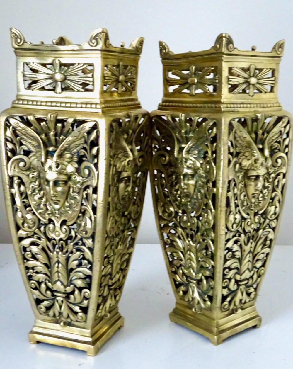 A pair of tall rectangular brass vases featuring pierced openwork scrolling foliage and central winged face motifs. View V