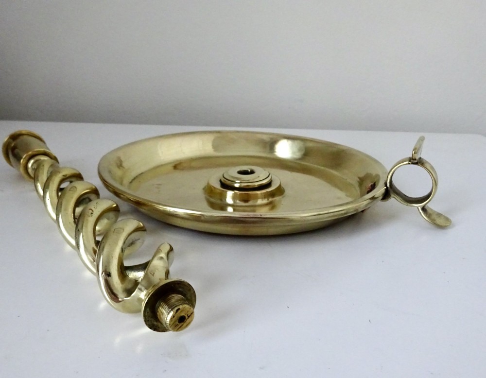 A polished brass chamberstick featuring an open barley twist stem set into a circular dish tray with a thumb ring handle. View II