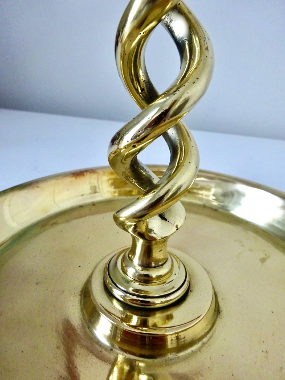 A polished brass chamberstick featuring an open barley twist stem set into a circular dish tray with a thumb ring handle. View III