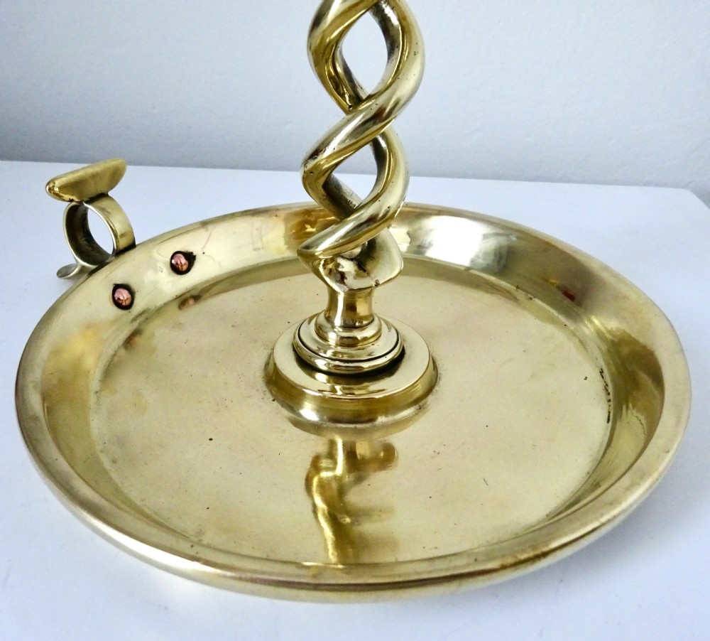 A polished brass chamberstick featuring an open barley twist stem set into a circular dish tray with a thumb ring handle. View IV