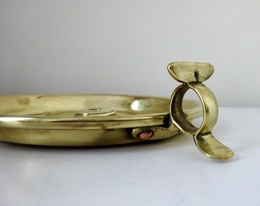 A polished brass chamberstick featuring an open barley twist stem set into a circular dish tray with a thumb ring handle. View VIII
