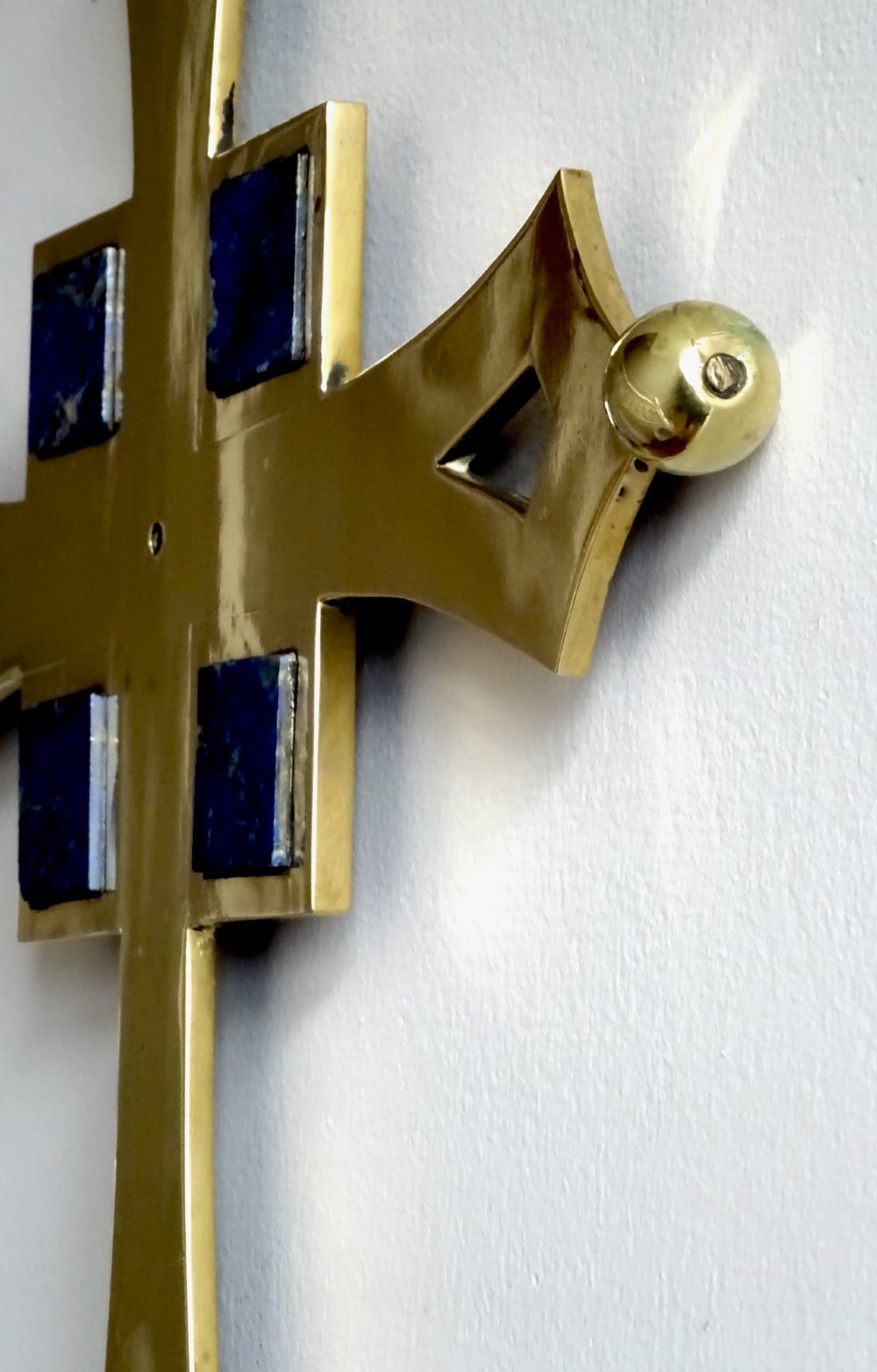 An Art Deco polished brass cross featuring flared arms with diamond cut-outs, ball finials, and four square lapis lazuli stone inlays at the centre. View VII