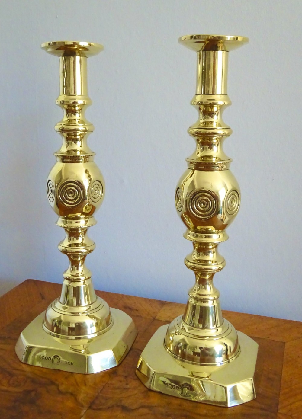A pair of polished late Victorian cast brass candlesticks featuring knopped stems and octagonal bases stamped with the words Good Luck alongside a horseshoe motif.