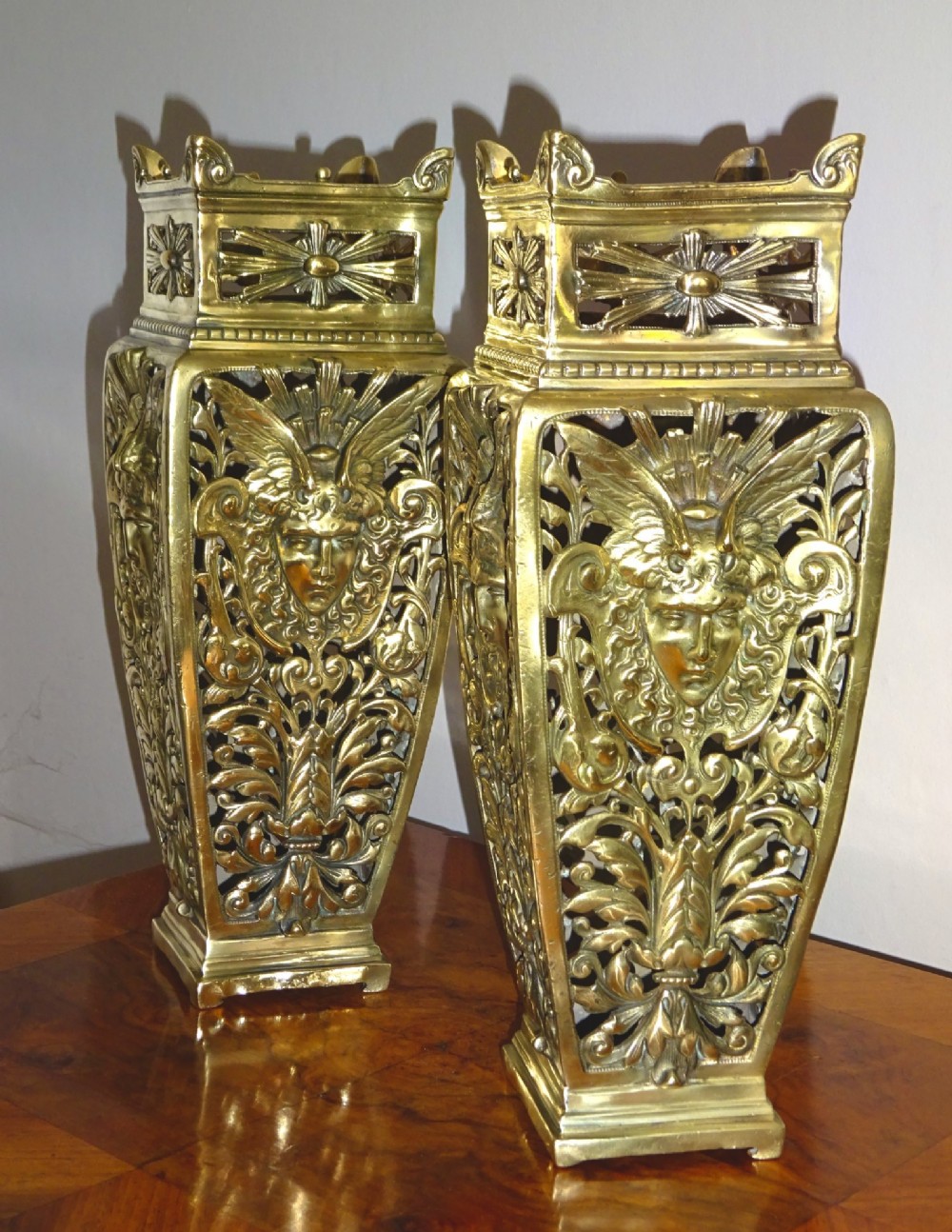 A pair of tall rectangular brass vases featuring pierced openwork scrolling foliage and central winged face motifs. View VIII