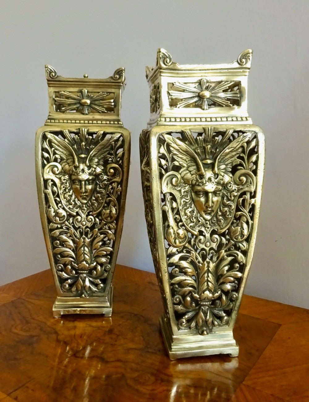 A pair of tall rectangular brass vases featuring pierced openwork scrolling foliage and central winged face motifs. View IX