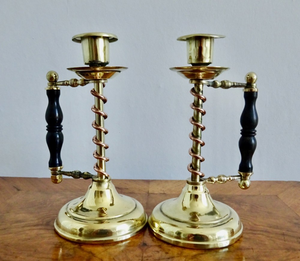 A pair of Edwardian Arts and Crafts brass candlesticks featuring spiral copper accents along the stems and turned dark wood side handles on circular brass bases. View II