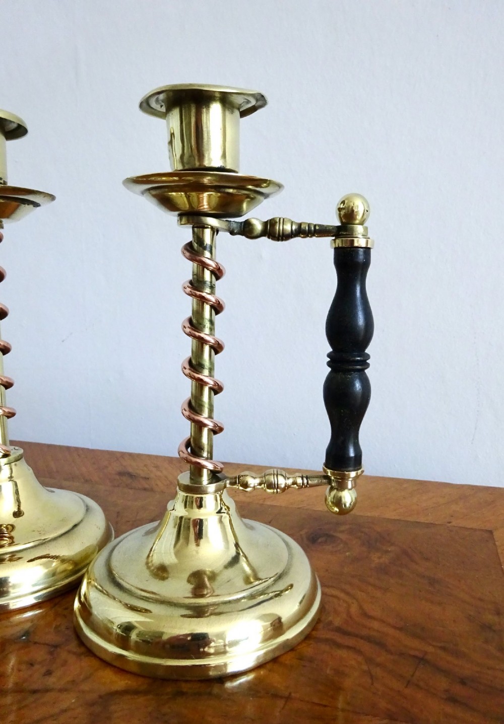A pair of Edwardian Arts and Crafts brass candlesticks featuring spiral copper accents along the stems and turned dark wood side handles on circular brass bases. View IV