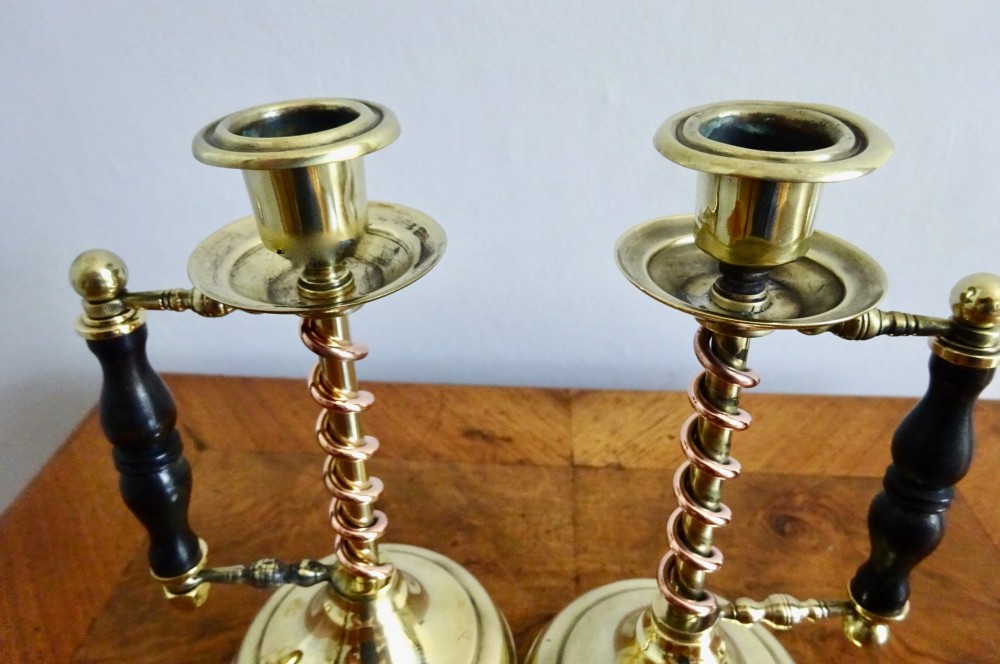 A pair of Edwardian Arts and Crafts brass candlesticks featuring spiral copper accents along the stems and turned dark wood side handles on circular brass bases. View V