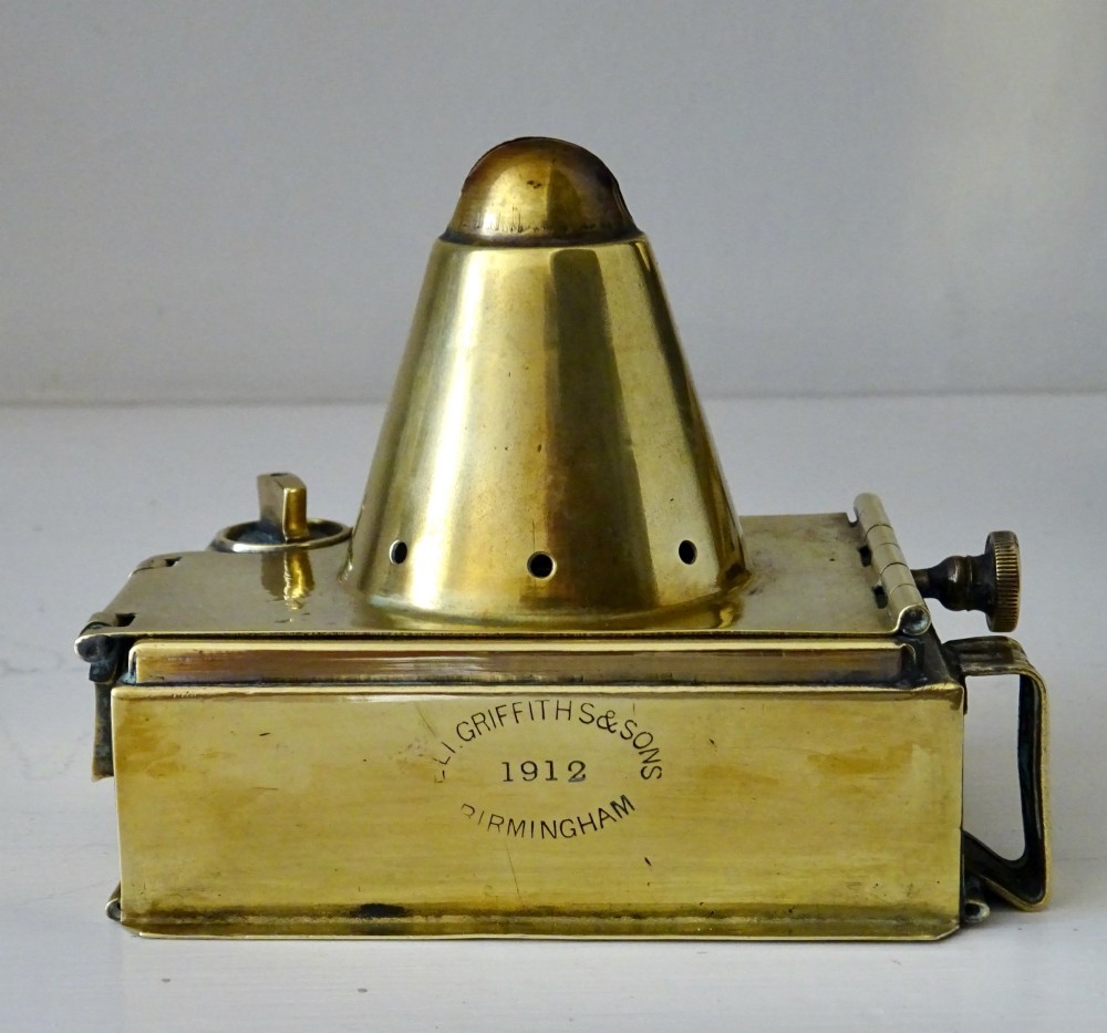 An antique brass oil lantern featuring a rectangular glass window, perforated ventilation top, turned wooden handle, and stamped manufacturer markings. View II