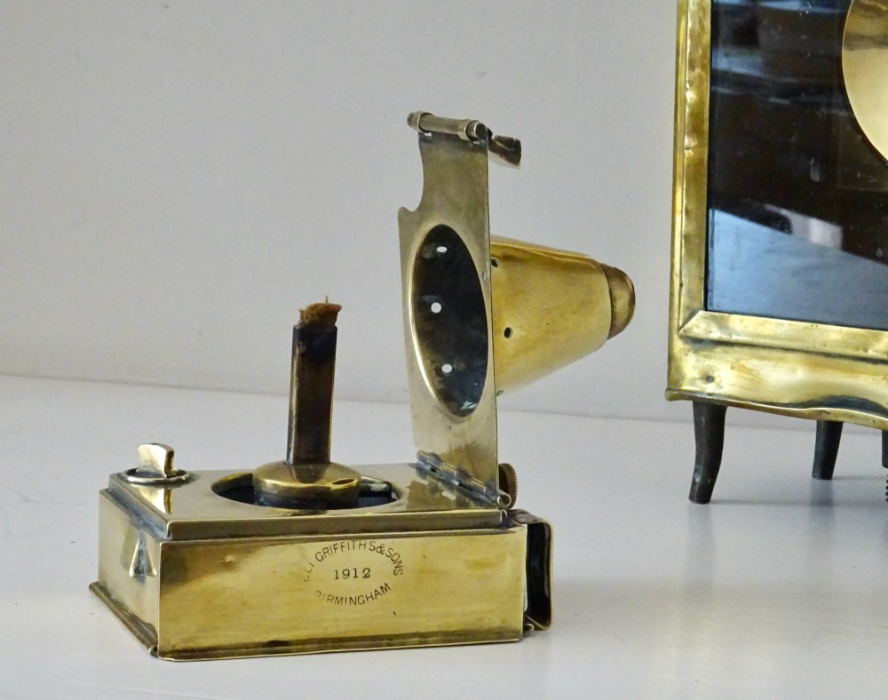 An antique brass oil lantern featuring a rectangular glass window, perforated ventilation top, turned wooden handle, and stamped manufacturer markings. View III