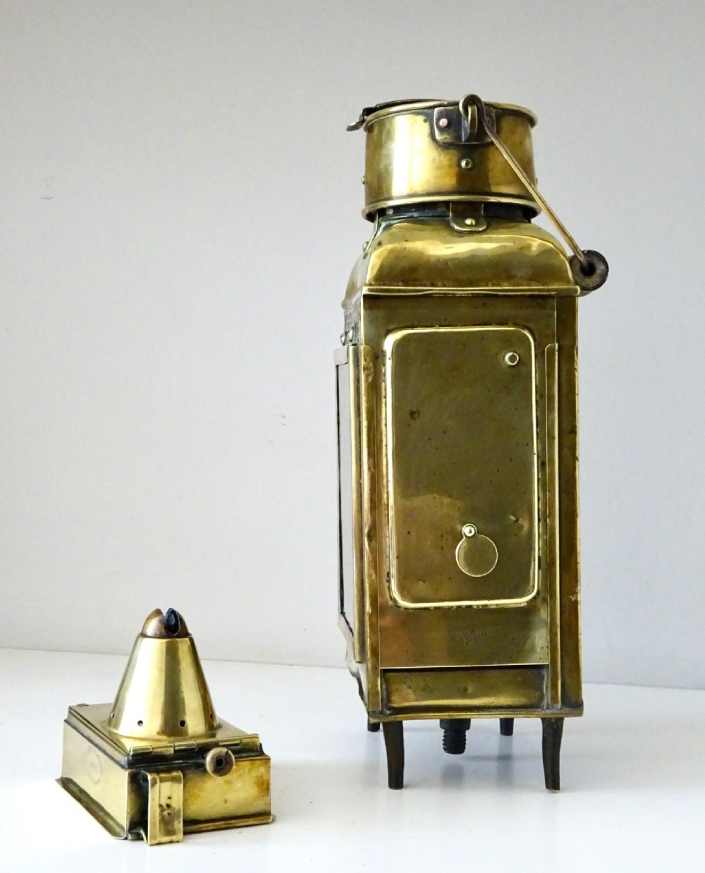 An antique brass oil lantern featuring a rectangular glass window, perforated ventilation top, turned wooden handle, and stamped manufacturer markings. View IV