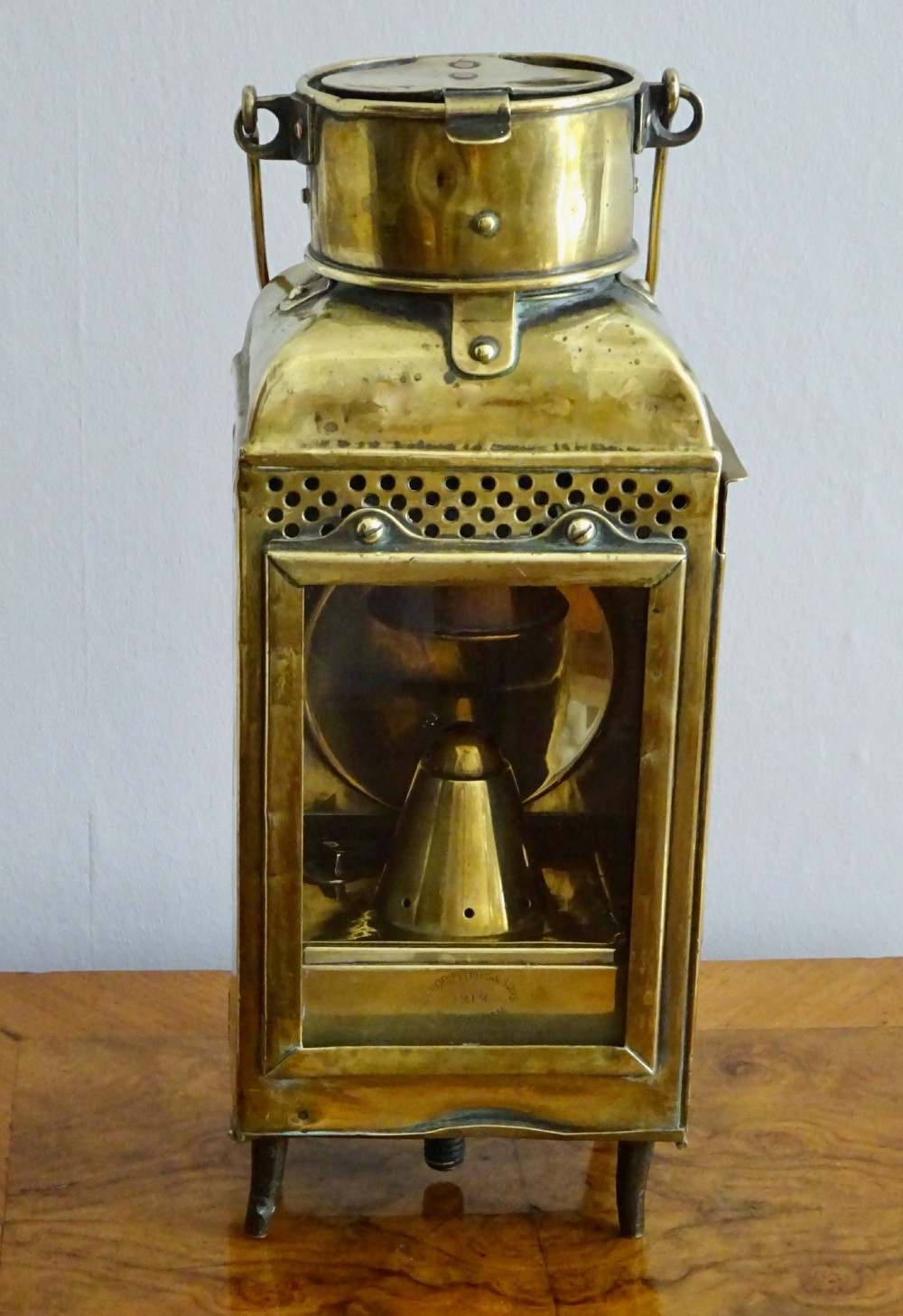 An antique brass oil lantern featuring a rectangular glass window, perforated ventilation top, turned wooden handle, and stamped manufacturer markings. View VIII
