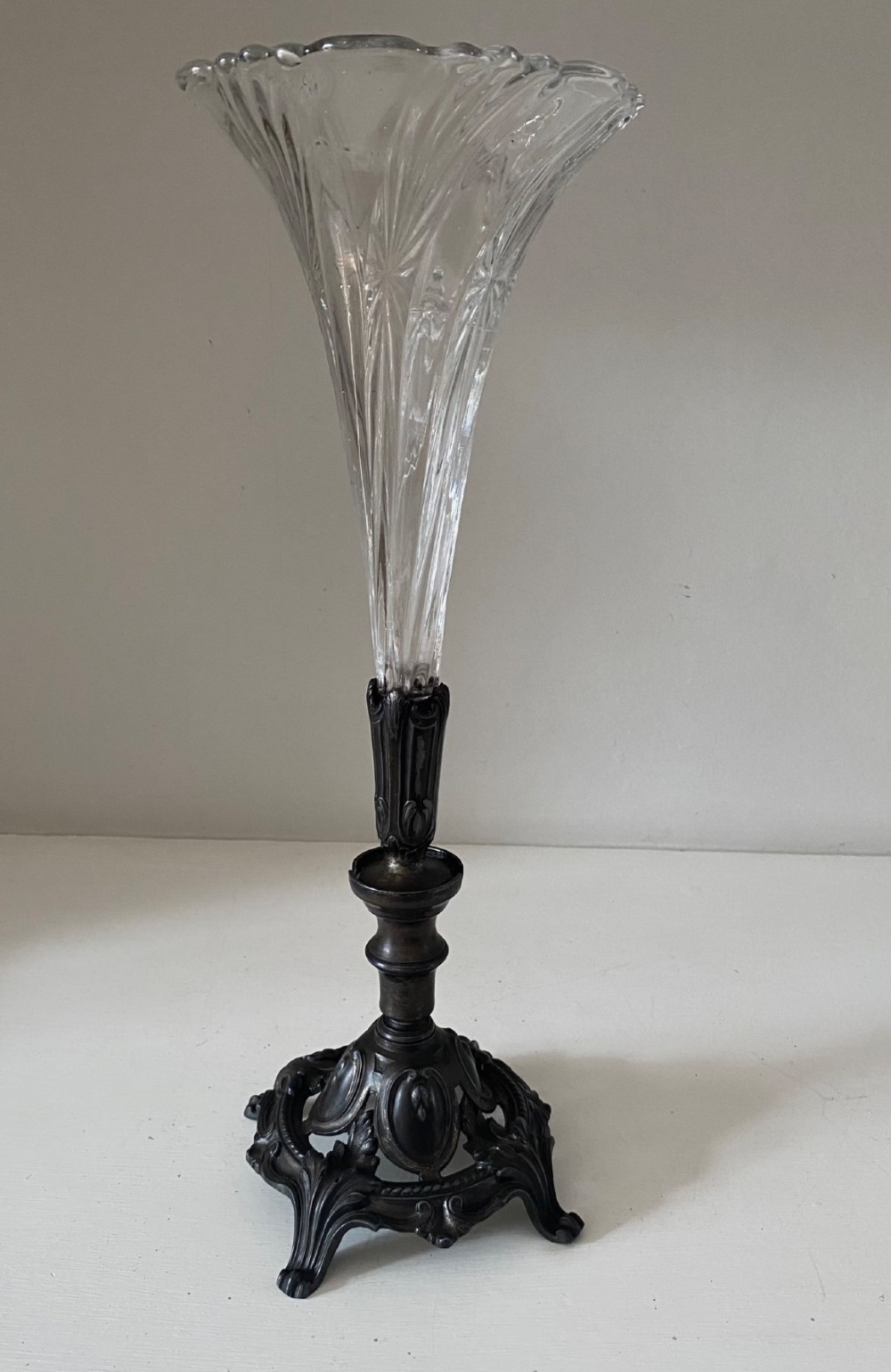 An antique single-trumpet epergne featuring a fluted clear glass vase fitted into an ornate dark cast-spelter base.