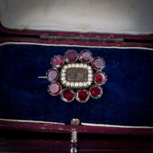 fig 3. A Georgian cluster brooch featuring flat-cut red garnets surrounding a halo of seed pearls and a central hairwork compartment set in gold.