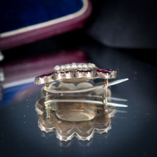 fig 4. A Georgian cluster brooch featuring flat-cut red garnets surrounding a halo of seed pearls and a central hairwork compartment set in gold.