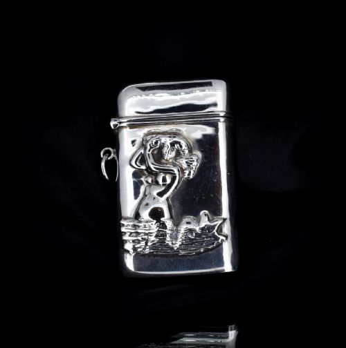 fig 2. A small rectangular sterling silver vesta case featuring an embossed repousse motif of a mermaid on water, held in a hand.