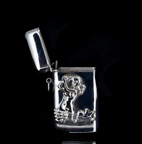 fig 1. A small rectangular sterling silver vesta case featuring an embossed repousse motif of a mermaid on water, held in a hand.