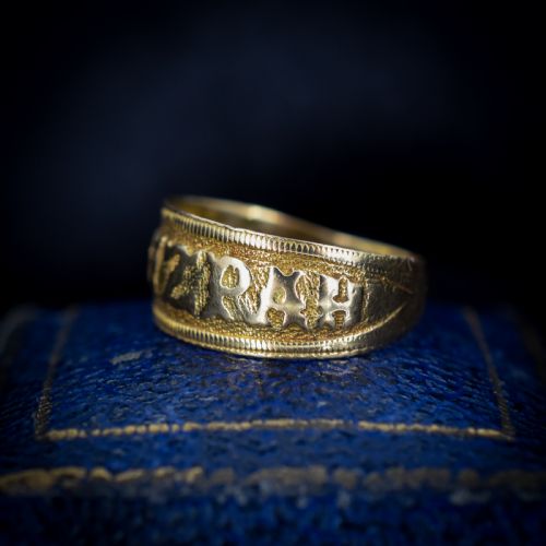 fig 2. A wide yellow gold band ring featuring raised lettering spelling MIZPAH against a textured background with milled borders.