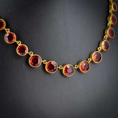 fig 1. An Edwardian gold gilt riviere necklace featuring round, bezel-set facetted red paste stones connected by fine metal links.