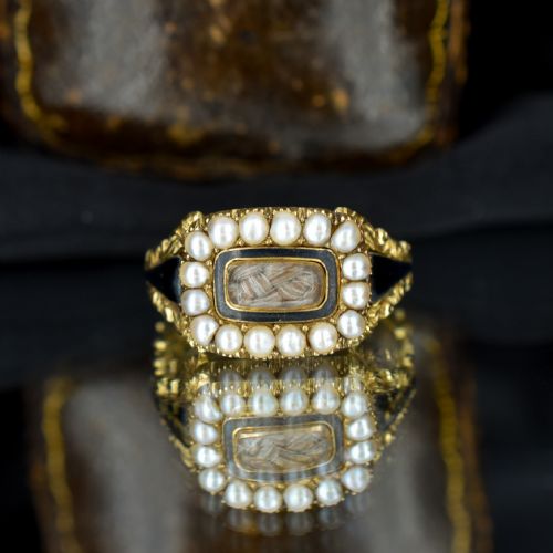 fig 1. An antique 18ct gold Georgian mourning ring featuring a central woven hair compartment framed by black enamel and a border of seed pearls.